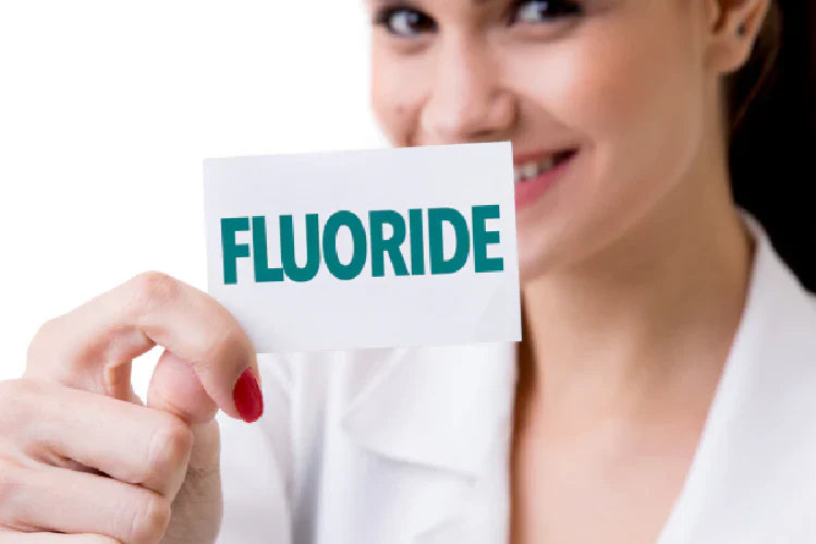 Een afbeelding van een vrouw die een kaarden vasthoudt waarop fluoride is geschreven.